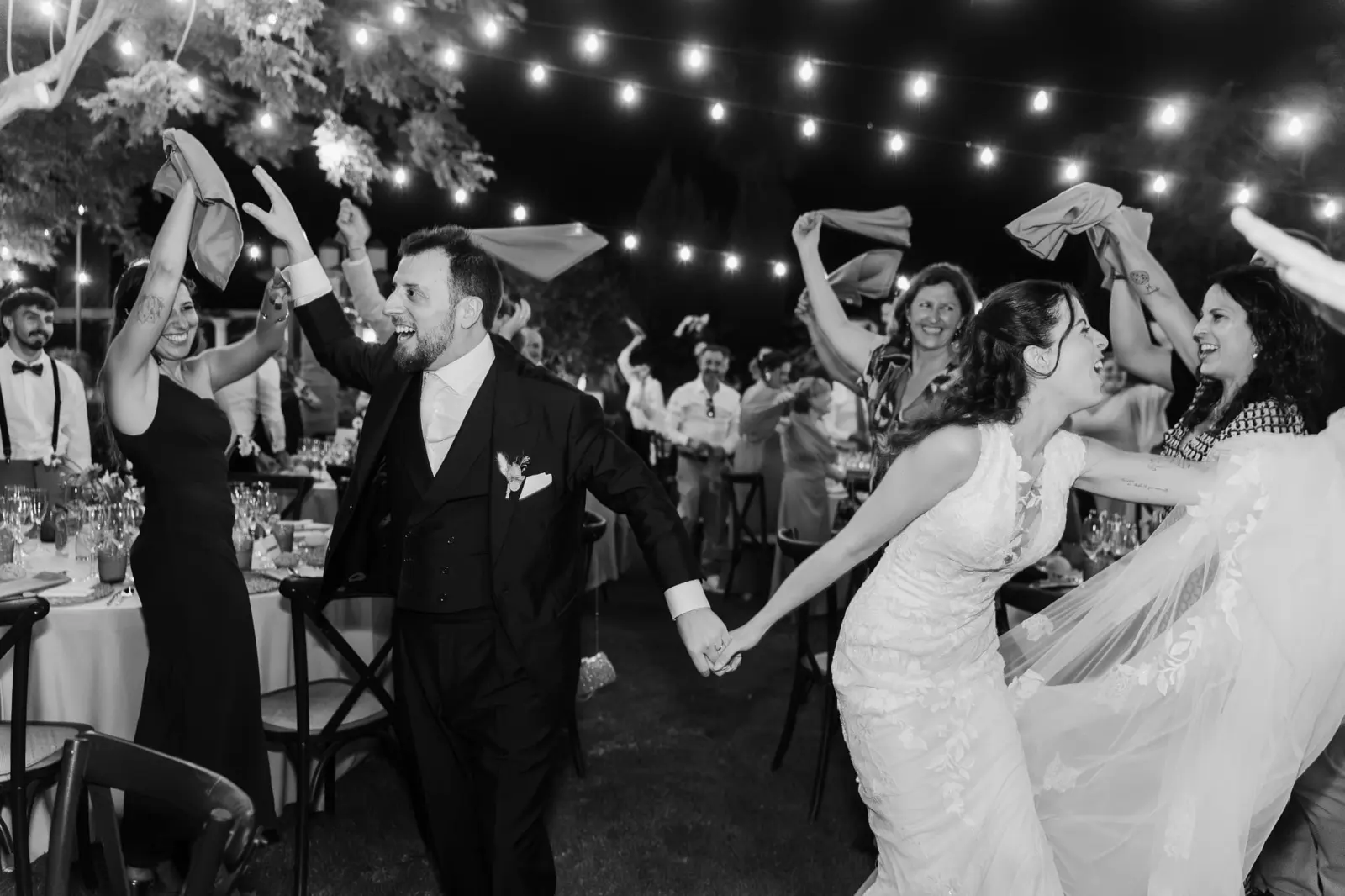 Ana y Manuel entrando al banquete entre invitados que agitan las servilletas, en blanco y negro