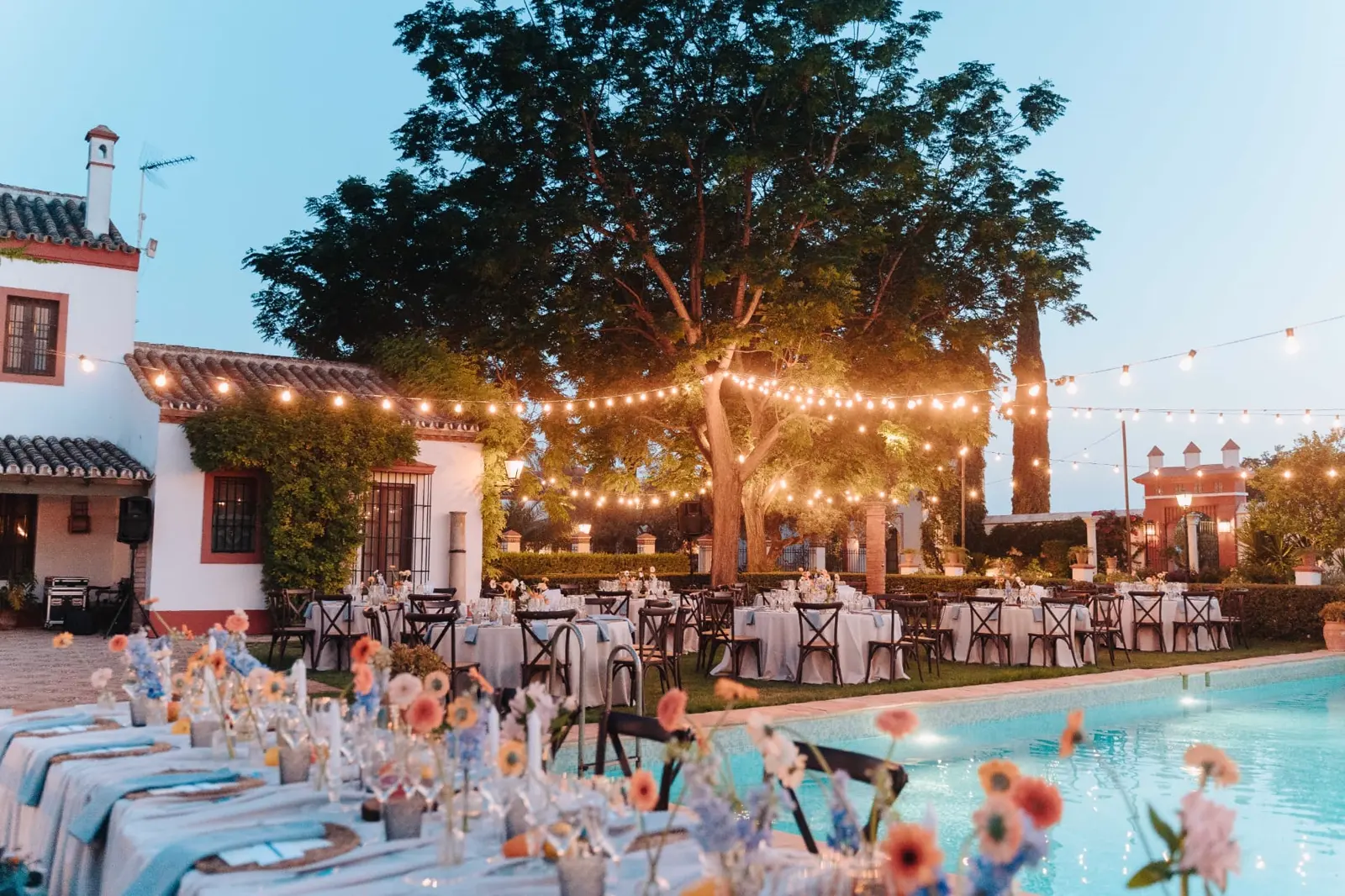 Montaje del banquete junto a la piscina con guirnaldas de luces al atardecer en Hacienda de Orán