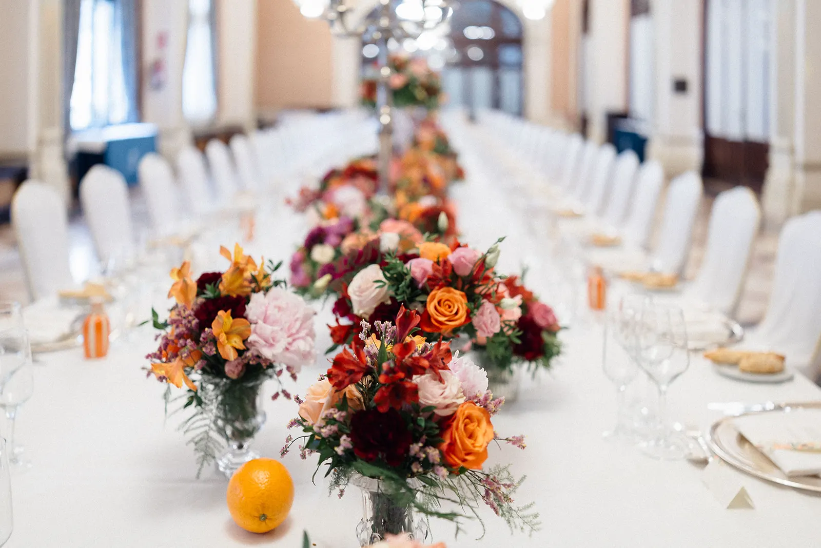 Mesa imperial con centros de flores de temporada y naranjas sobre mantel blanco