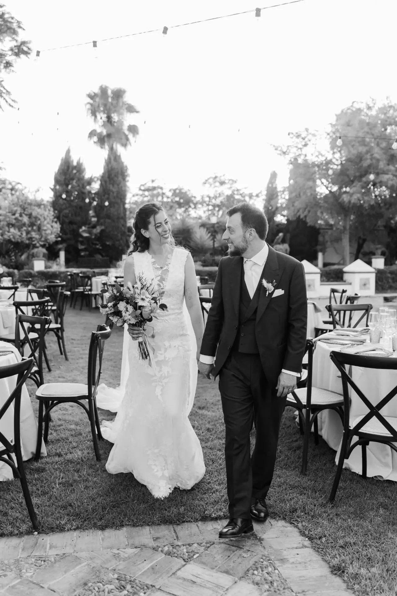 Ana y Manuel paseando entre las mesas del jardín y mirándose, en blanco y negro