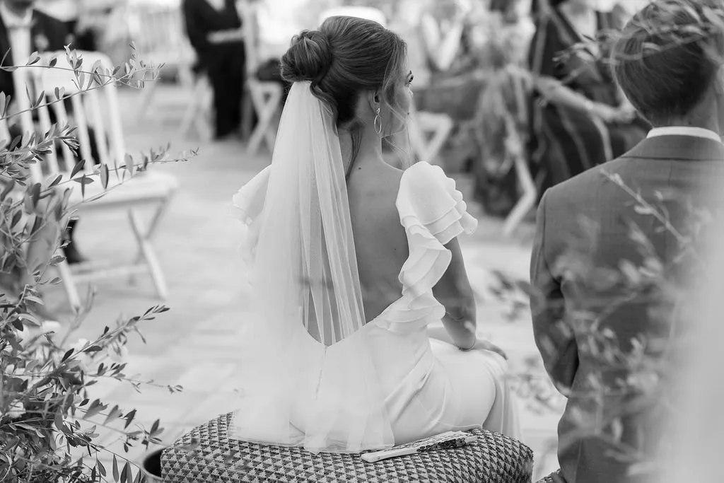 Julia con velo durante la ceremonia entre olivos, en blanco y negro