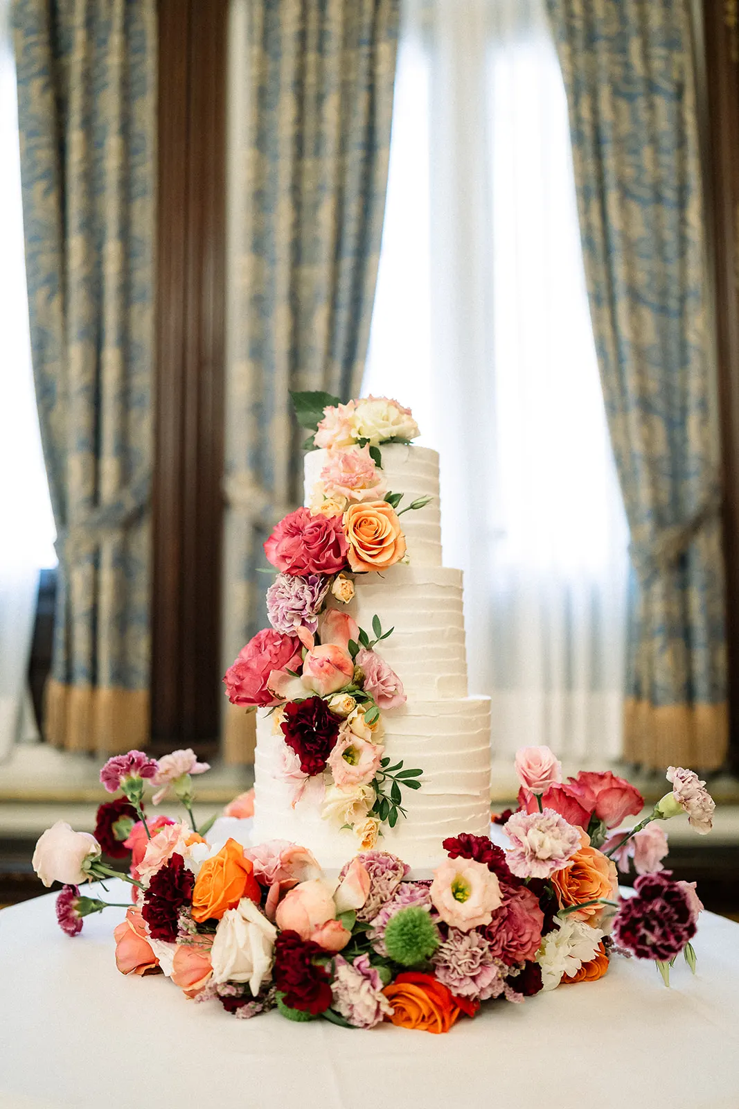 Tarta nupcial de tres pisos decorada con flores en tonos coral, rosa y granate