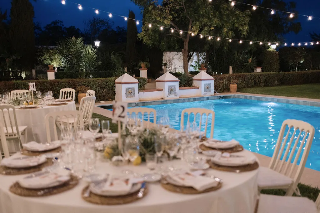 Banquete junto a la piscina iluminada bajo guirnaldas de luces
