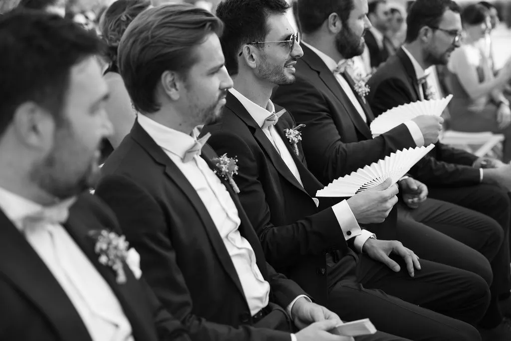 Invitados con abanicos durante la ceremonia de Julia y Paul, en blanco y negro