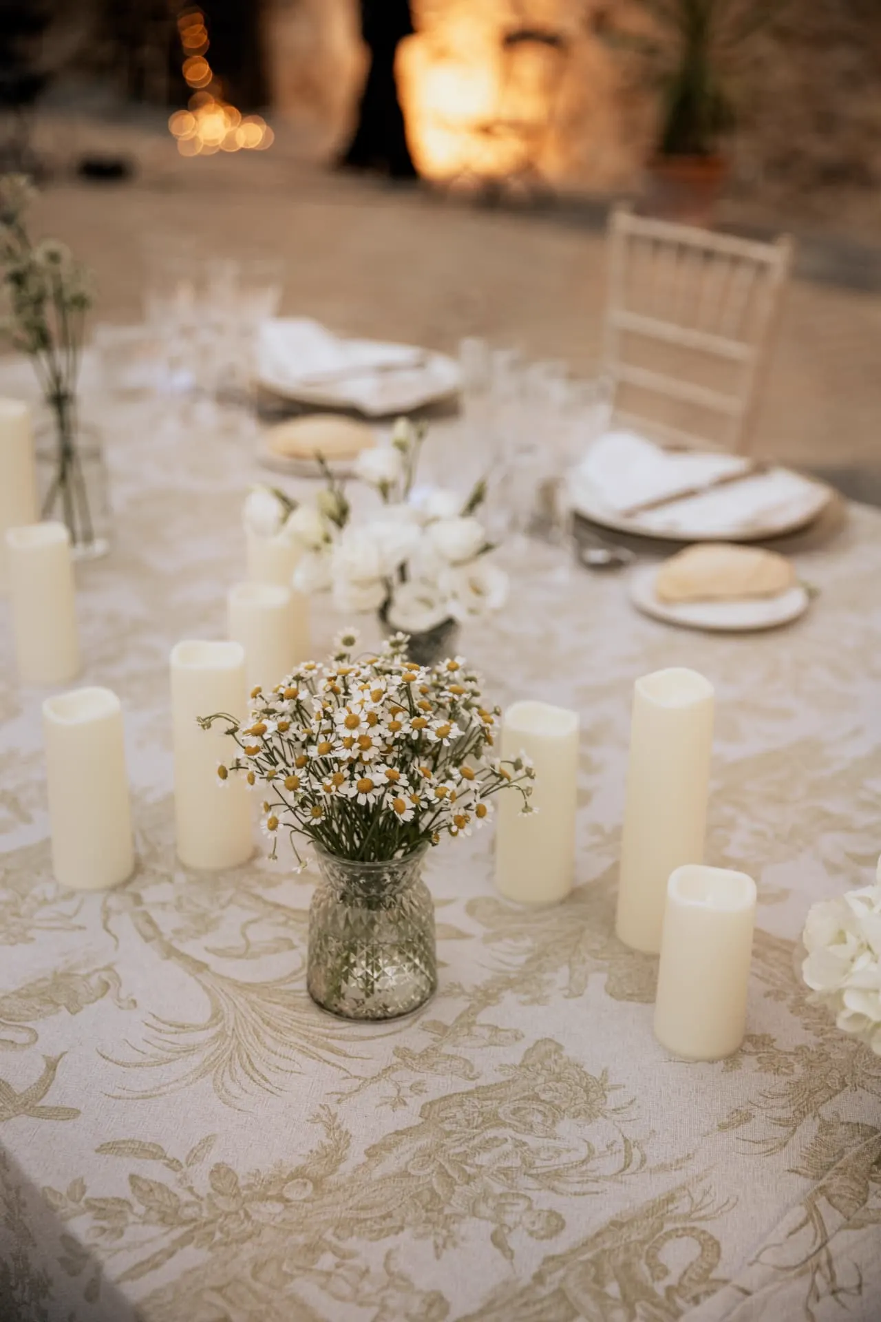 Centro de mesa con margaritas silvestres y velas sobre mantel de damasco