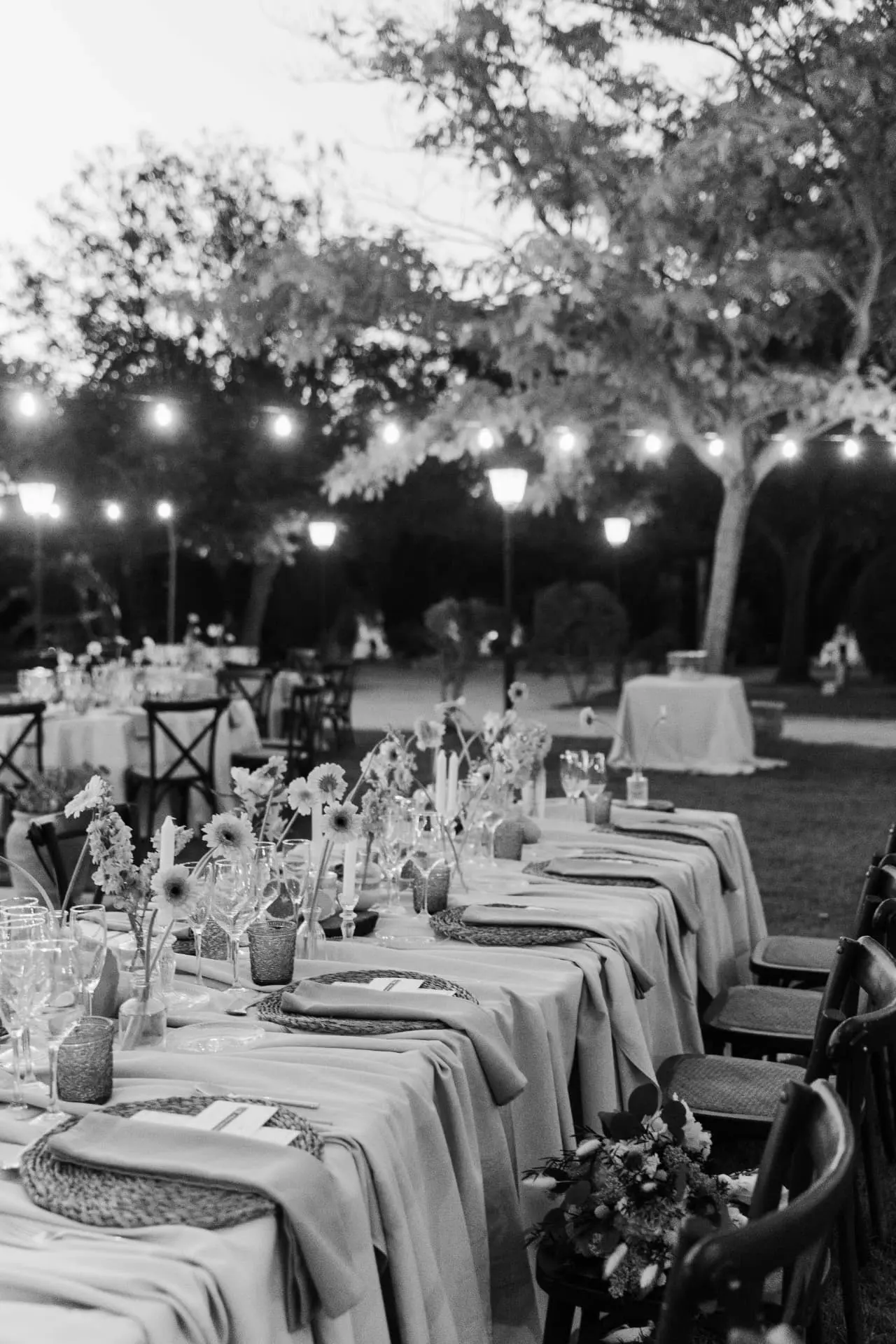 Detalle en blanco y negro de la mesa larga del banquete en el jardín al anochecer