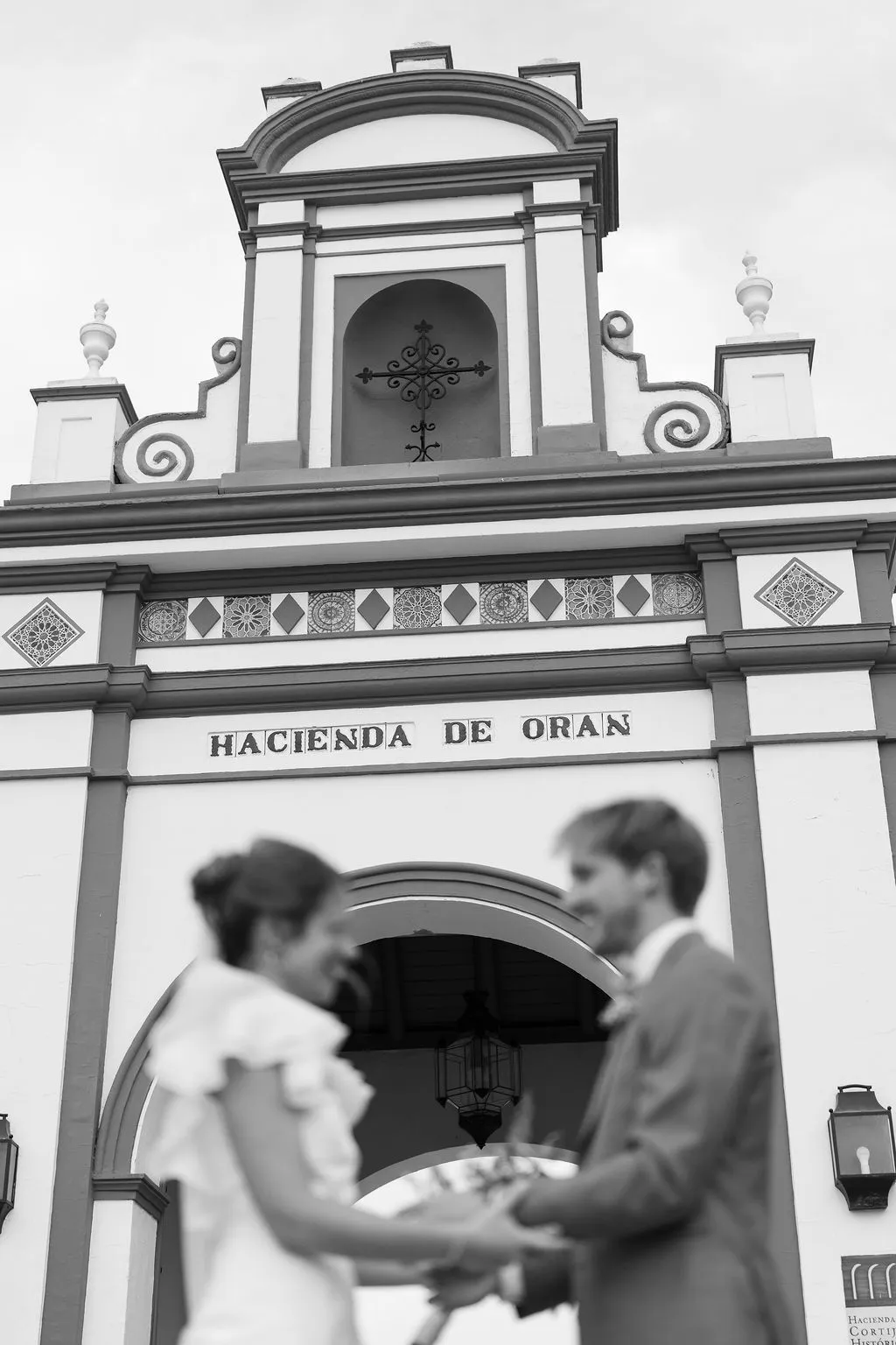 Julia y Paul de la mano frente a la portada de Hacienda de Orán, en blanco y negro