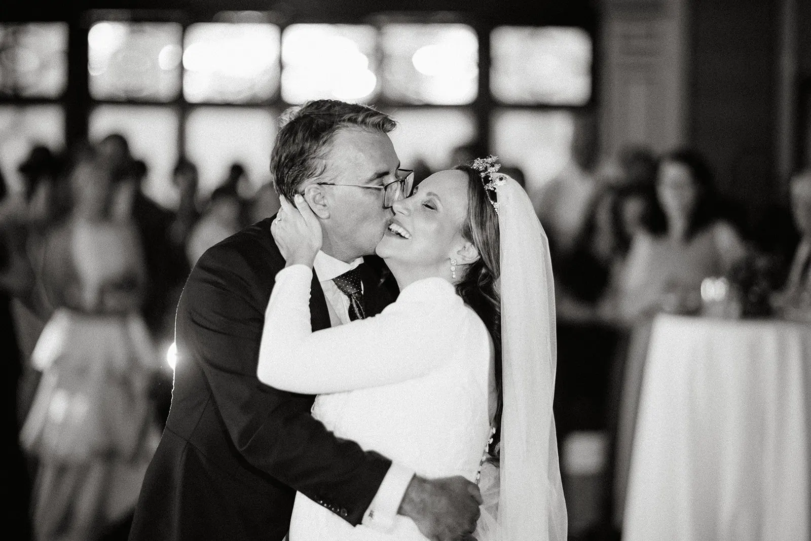 Beso de Luyza y Fernando durante el baile rodeados de invitados, en blanco y negro