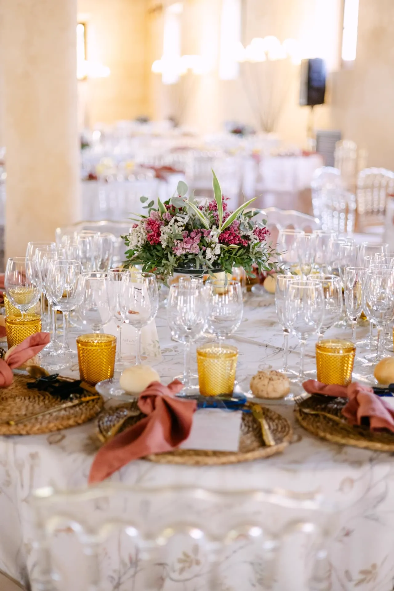 Mesa del banquete con centro floral en tonos rosas, cristalería y servilletas terracota