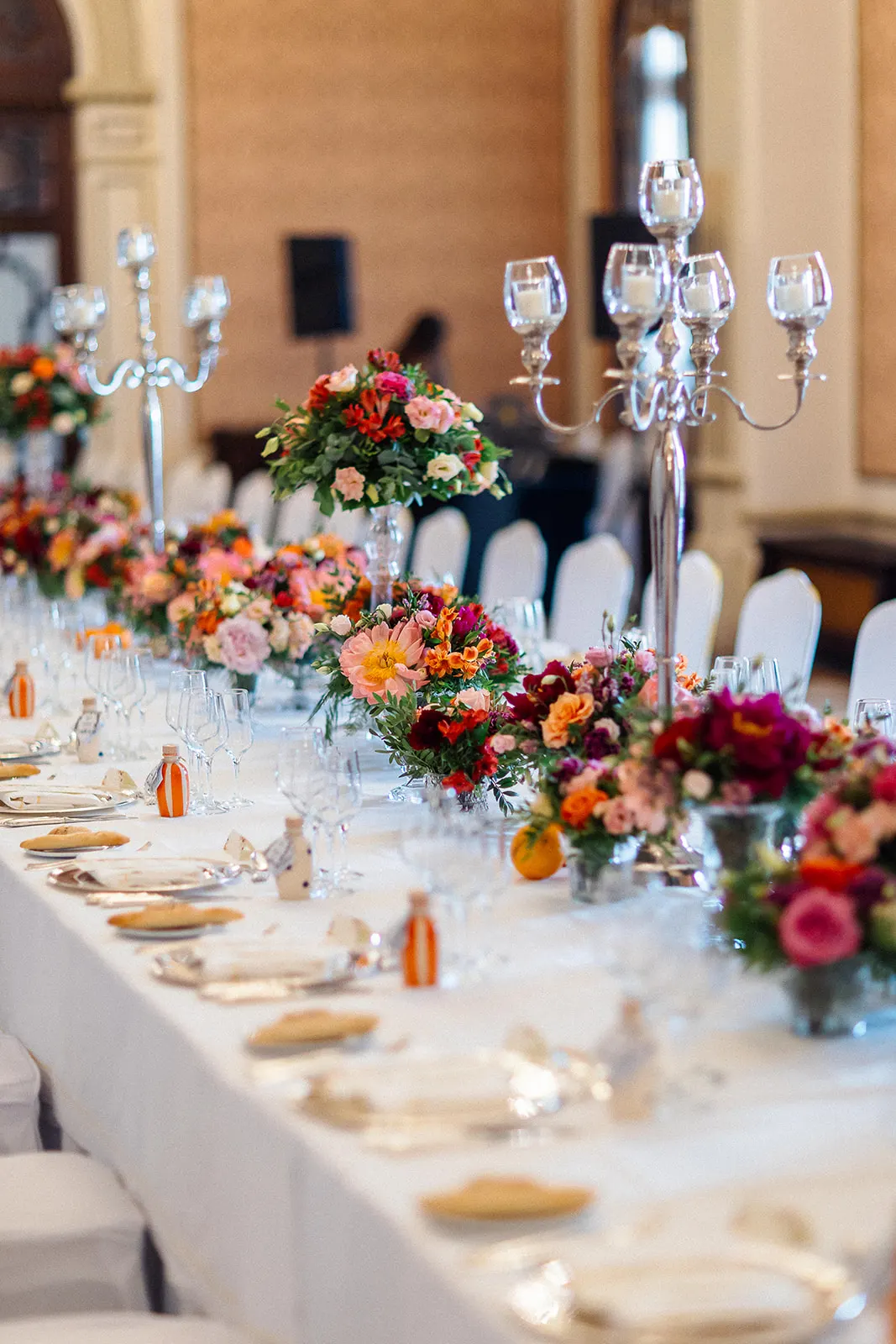 Mesa larga con candelabros de plata y centros florales en tonos coral y granate