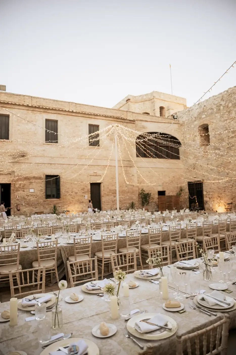 Montaje de mesas largas con mantelería de damasco en el patio del castillo